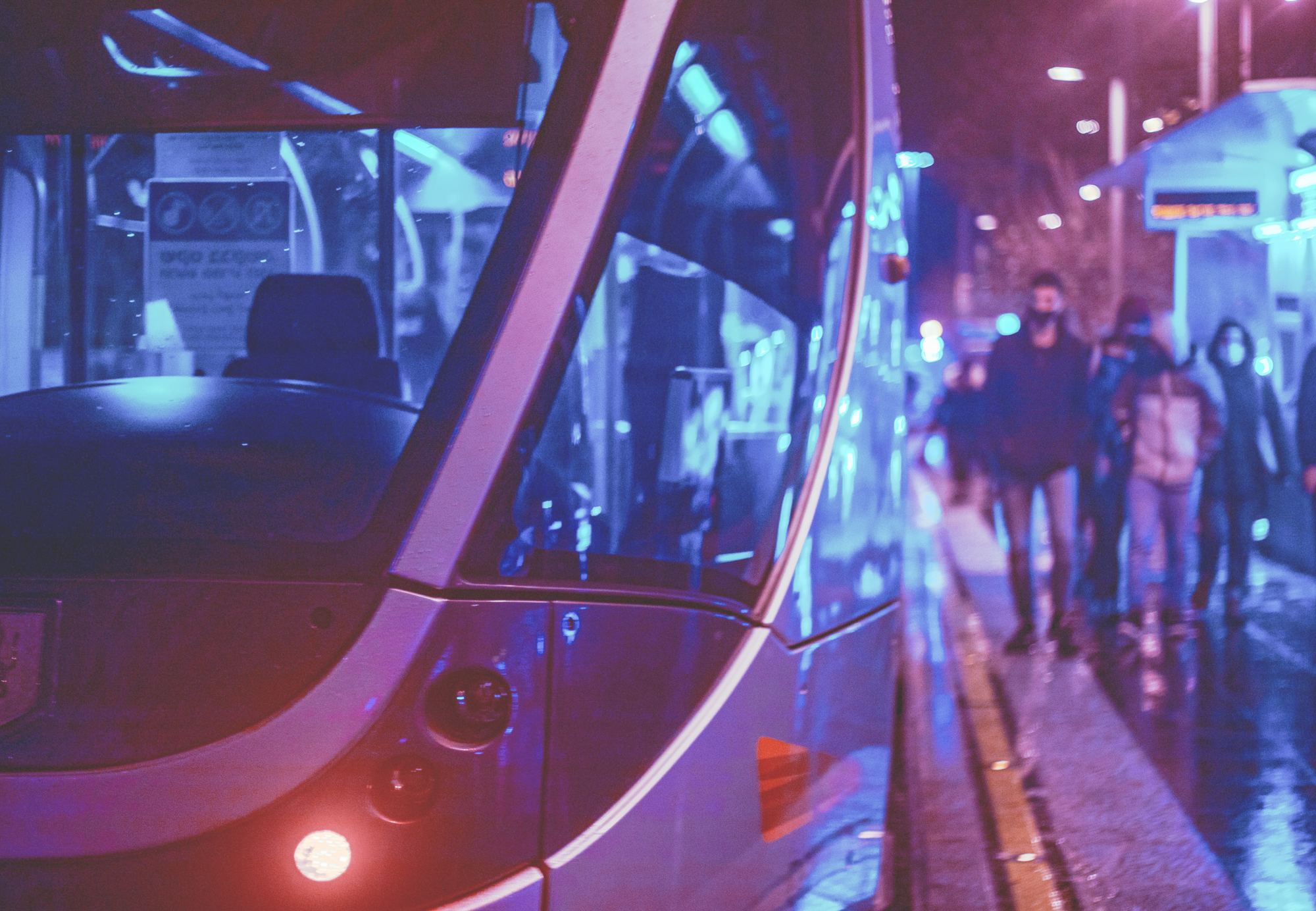 outdoor photo of public transportation and people at night with purple and blue lighting